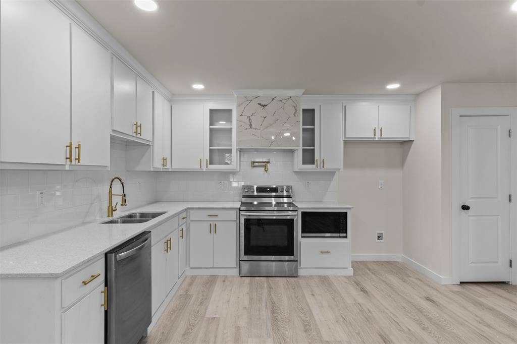 106 Mount Shasta Street, Dallas, TX 75211 White cabinetry with gold-finish hardware, stainless steel appliances, a tile backsplash, and wood-finish flooring