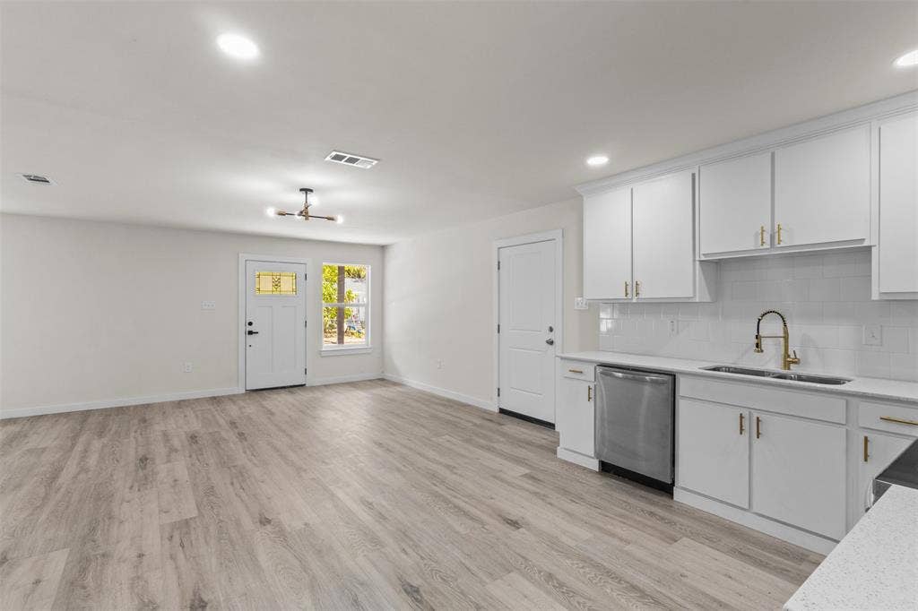 106 Mount Shasta Street, Dallas, TX 75211 Wood-finish flooring throughout, recessed lighting, white kitchen cabinetry with gold-finish hardware, stainless steel dishwasher, and a white subway tile backsplash