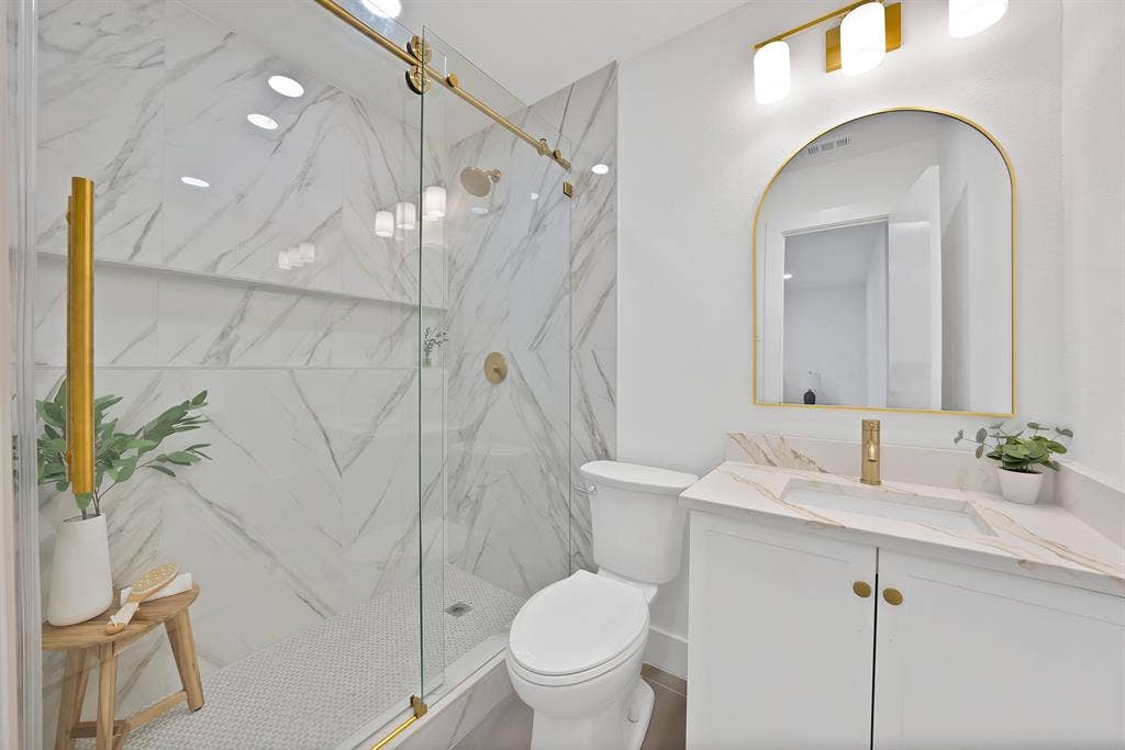 132 Yorkshire Drive, Cedar Hill, TX 75104 Contemporary bathroom featuring a spacious glass-enclosed shower with gold-finish hardware, white hexagonal tile flooring, and marble-look tile walls