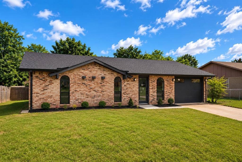 132 Yorkshire Drive, Cedar Hill, TX 75104 Brick exterior featuring a dark asphalt shingle roof, arched front windows, a black garage door, and a concrete driveway