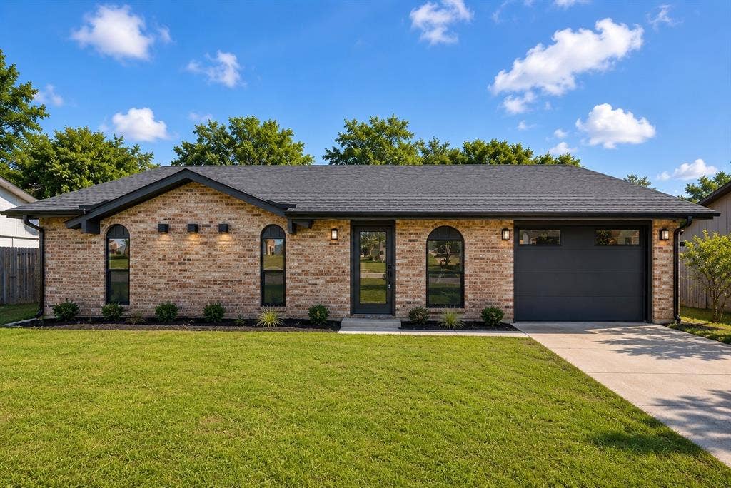 132 Yorkshire Drive, Cedar Hill, TX 75104 Brick exterior featuring a dark asphalt shingle roof, black framed arched windows, black garage door, and a concrete driveway