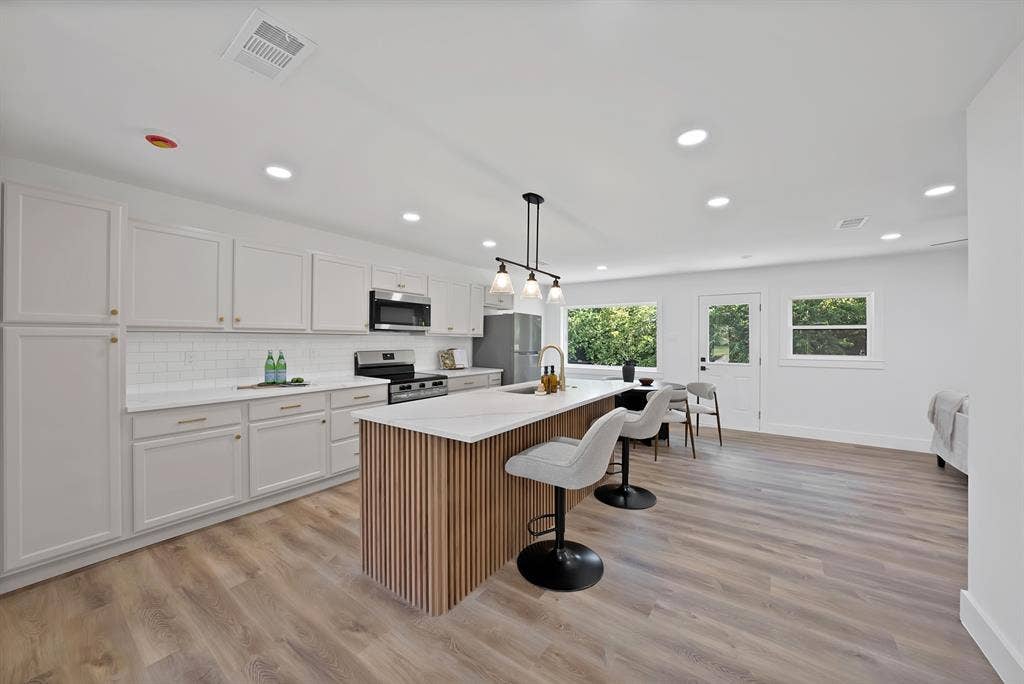 132 Yorkshire Drive, Cedar Hill, TX 75104 Open-concept kitchen featuring an island with a wood-slat base, quartz countertops, white shaker cabinetry, a subway tile backsplash, and stainless steel appliances