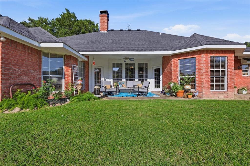 510 Saralvo Road, Midlothian, TX 76065 Expansive backyard featuring a manicured lawn, a covered patio, brick exterior, large windows, and mature landscaping