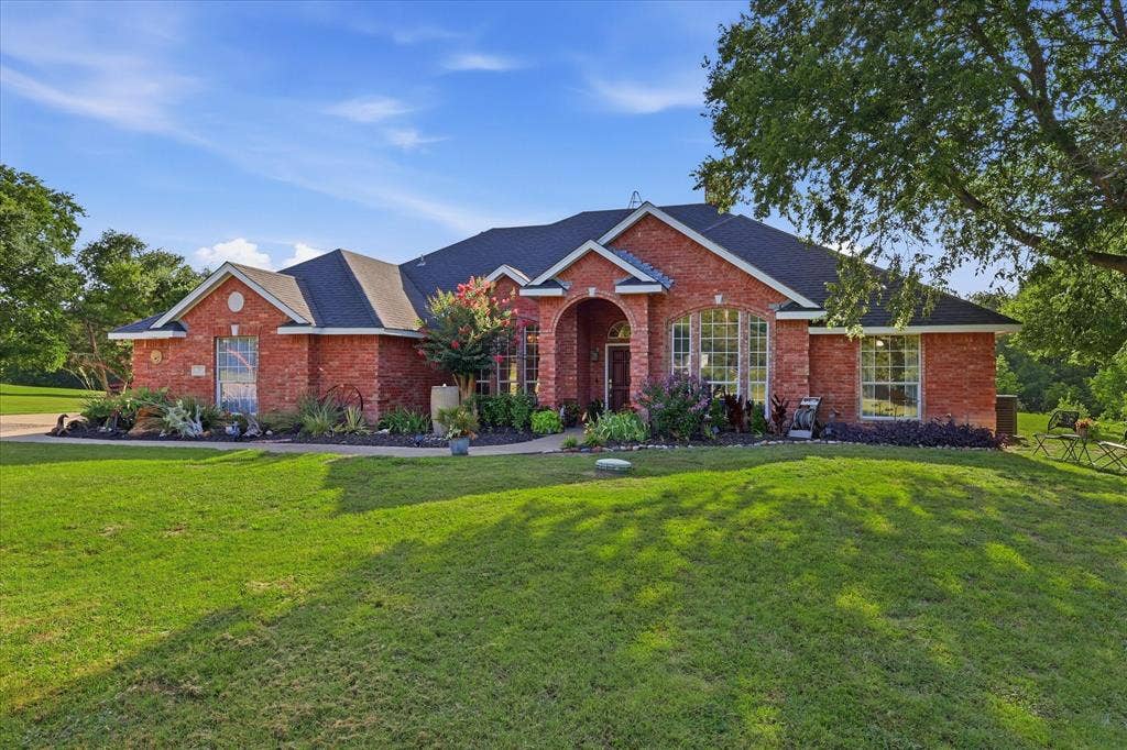 510 Saralvo Road, Midlothian, TX 76065 Red brick exterior with a dark shingle roof, arched entry, multiple large windows, and landscaped garden beds
