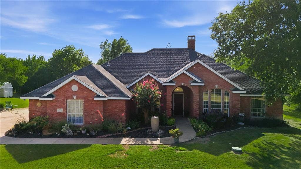 510 Saralvo Road, Midlothian, TX 76065 Brick residence featuring a prominent entryway arch, arched windows, a dark shingle roof, and mature landscaping