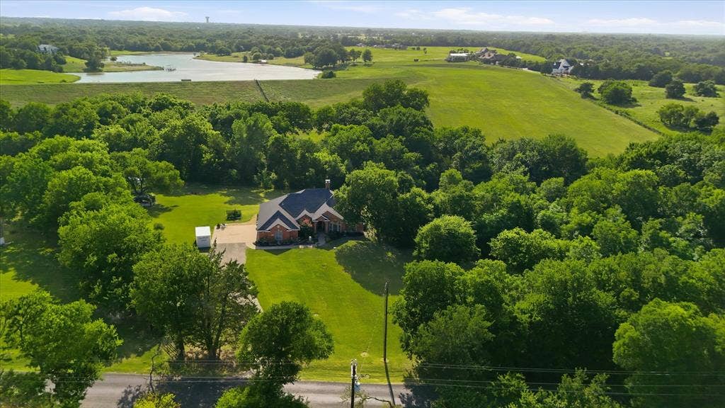 510 Saralvo Road, Midlothian, TX 76065 Sprawling property featuring a single-story brick residence with a dark roof and prominent gables, surrounded by mature trees and expansive green lawns