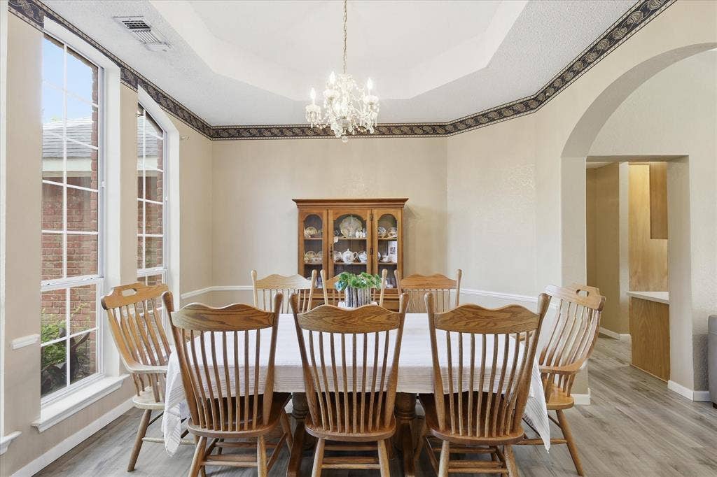 510 Saralvo Road, Midlothian, TX 76065 Dining area featuring a tray ceiling with decorative trim, large bay windows, a crystal chandelier, and wood-finish flooring