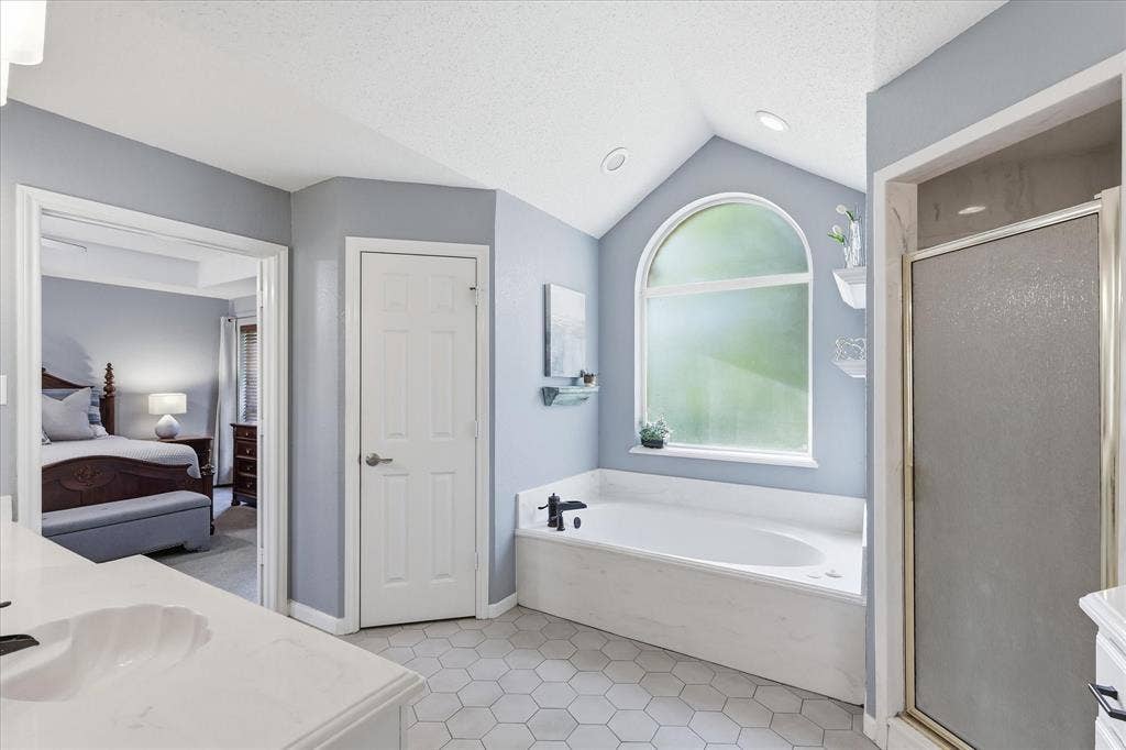 510 Saralvo Road, Midlothian, TX 76065 Bathroom featuring a built-in soaking tub under an arched window, a stand-up shower with a glass enclosure, and hexagonal tile flooring