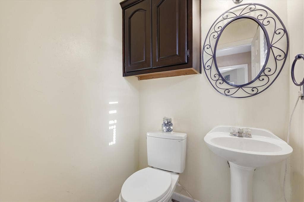 510 Saralvo Road, Midlothian, TX 76065 Pedestal sink with dual-handle chrome faucet, oval wall mirror with decorative metal frame, and wall-mounted dark wood cabinetry