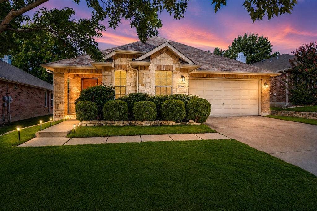 12841 Serenity Drive, Frisco, TX 75035 Stone and brick facade home featuring a two-car garage, mature landscaping, concrete driveway, and illuminated front walkway
