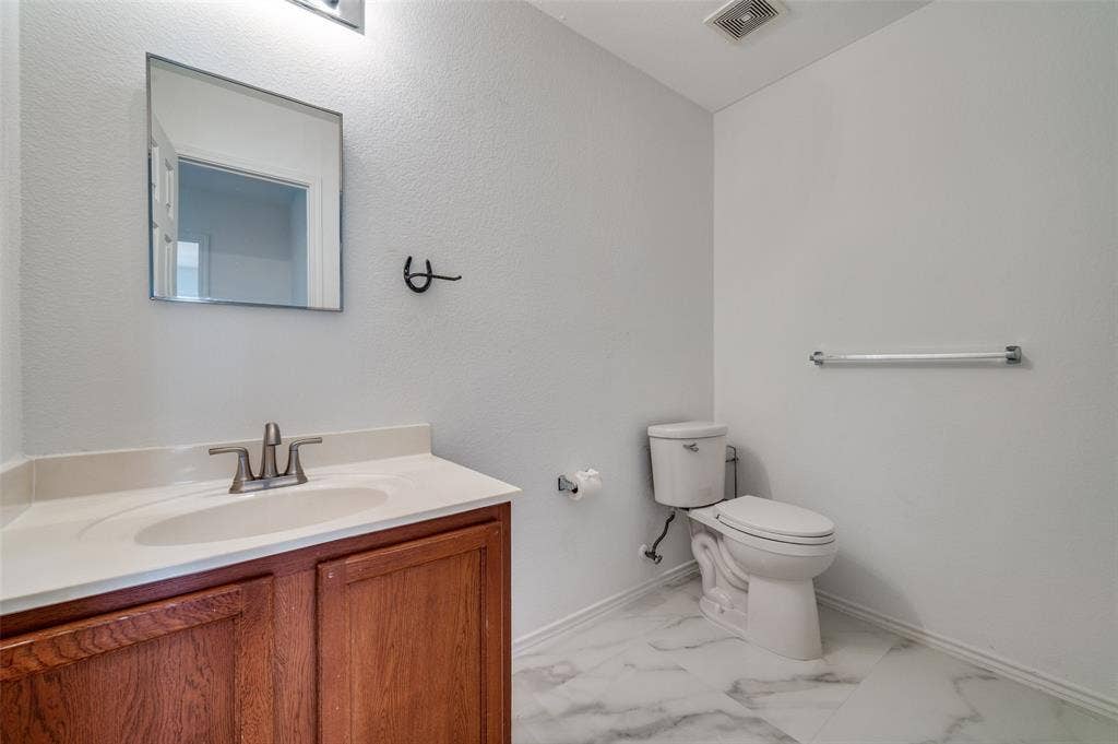 12841 Serenity Drive, Frisco, TX 75035 Bathroom featuring a wood-finish vanity with a light-toned countertop, a rectangular mirror, and marble-look floor tiling