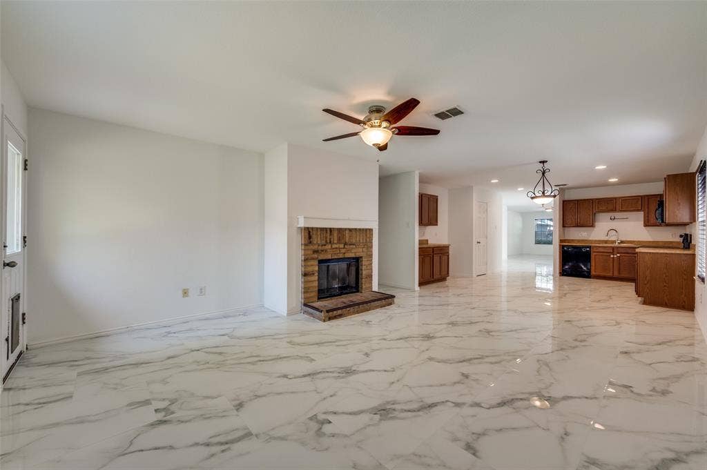 12841 Serenity Drive, Frisco, TX 75035 Open-concept living area with large-format marble-look tile flooring, a brick-surround fireplace with hearth, and a ceiling fan
