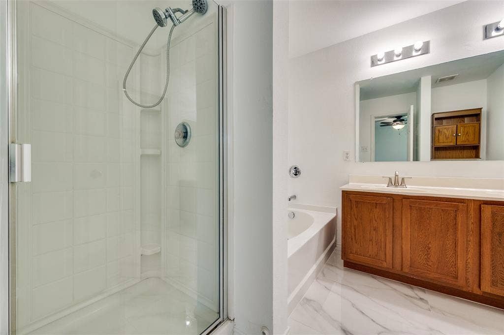 12841 Serenity Drive, Frisco, TX 75035 Bathroom featuring a glass-enclosed shower, an alcove bathtub, a long wood-finish vanity with ample storage, a large mirror, and marbling tile flooring