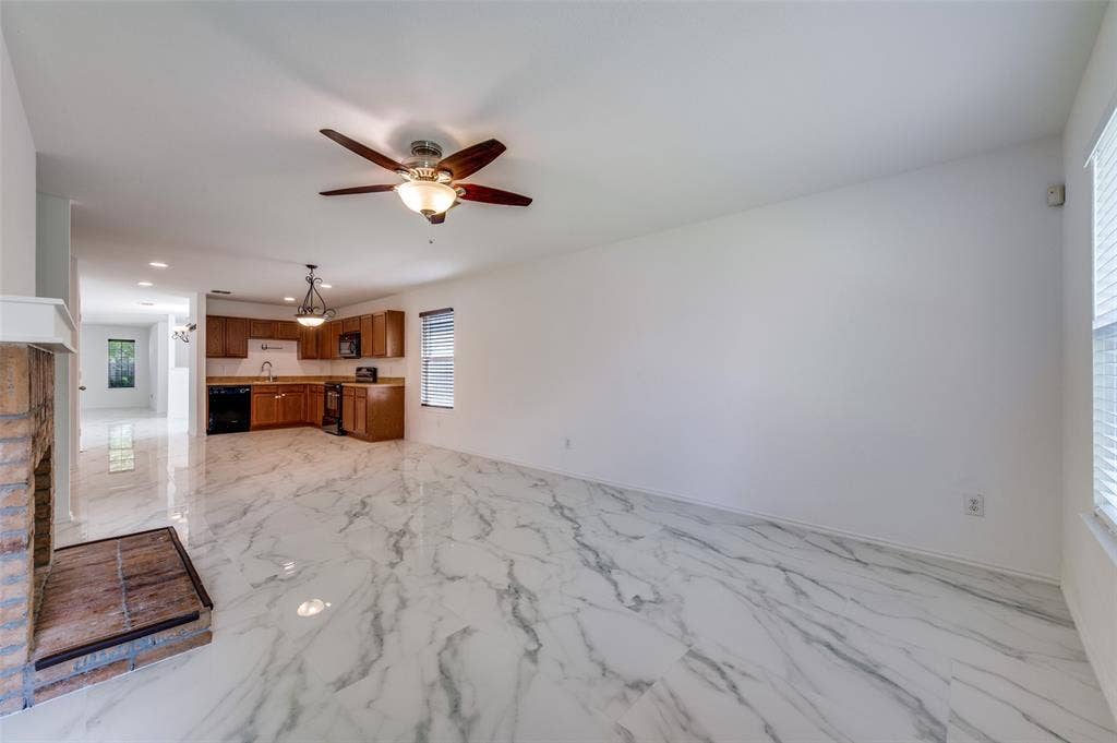 12841 Serenity Drive, Frisco, TX 75035 Open-concept living area featuring white marble-look flooring, a brick fireplace with a raised hearth, and a ceiling fan with integrated lighting
