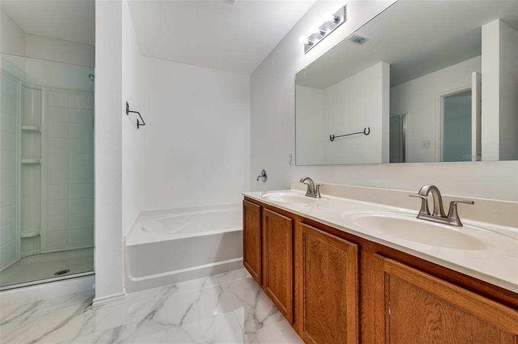12841 Serenity Drive, Frisco, TX 75035 Spacious bathroom featuring a double vanity with wood cabinetry, brushed nickel fixtures, a large integrated mirror, a separate shower enclosure, and a built-in tub