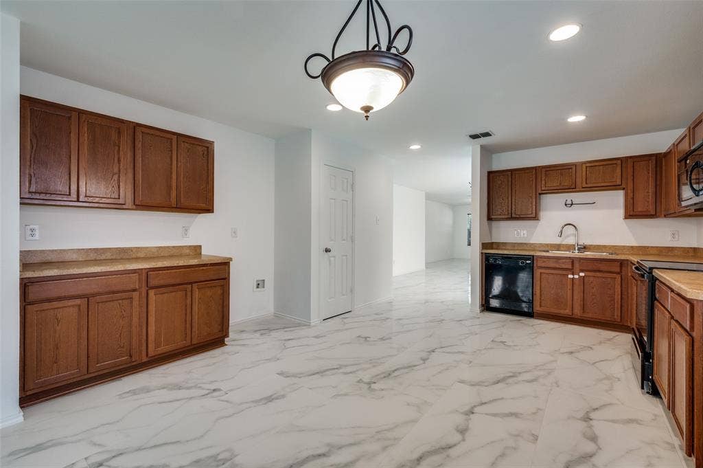 12841 Serenity Drive, Frisco, TX 75035 Spacious kitchen featuring sleek tile flooring, rich wood-finish cabinetry, and a black appliance suite