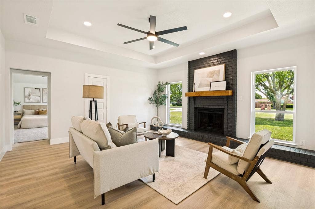 109 Shadow Drive, Red Oak, TX 75154 Living area featuring a tray ceiling with a ceiling fan, a dark brick fireplace with a wood mantle, wood-finish flooring, and white trim