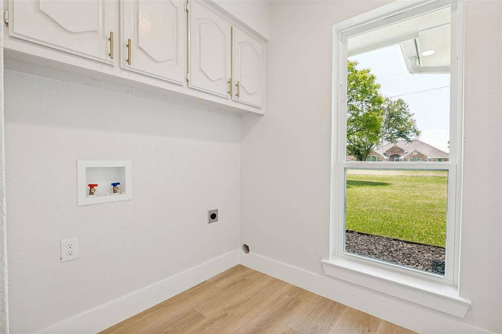 109 Shadow Drive, Red Oak, TX 75154 Laundry area with wood-finish flooring, white cabinetry with gold-tone hardware, and a single window