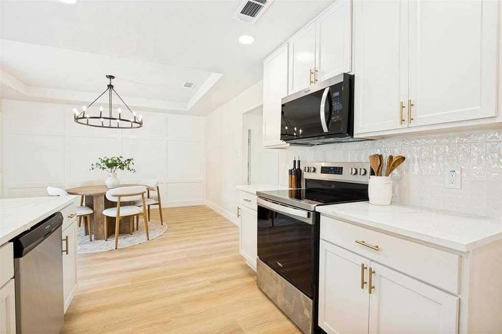 109 Shadow Drive, Red Oak, TX 75154 Open-concept kitchen and dining area featuring light wood-finish flooring, white cabinetry with gold-toned hardware, white countertops, and stainless steel appliances