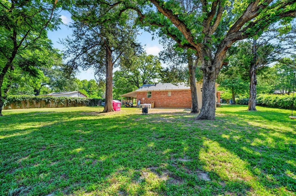 810 Edna Street, Athens, TX 75751 Expansive backyard featuring mature shade trees, a manicured lawn, and brick-façade residence with covered patio