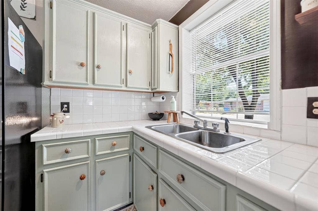 810 Edna Street, Athens, TX 75751 Kitchen featuring a double stainless steel sink with a window above, light green cabinetry, white tile countertops, and a white tile backsplash