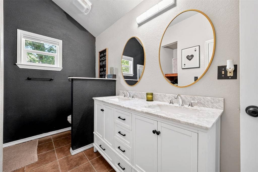 810 Edna Street, Athens, TX 75751 Double vanity featuring a white cabinet with black hardware, marble-finish countertop, and two oval mirrors with gold-tone frames