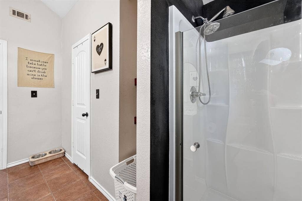 810 Edna Street, Athens, TX 75751 Shower enclosure featuring a chrome showerhead with a handheld sprayer, white paneling, and a clear glass door