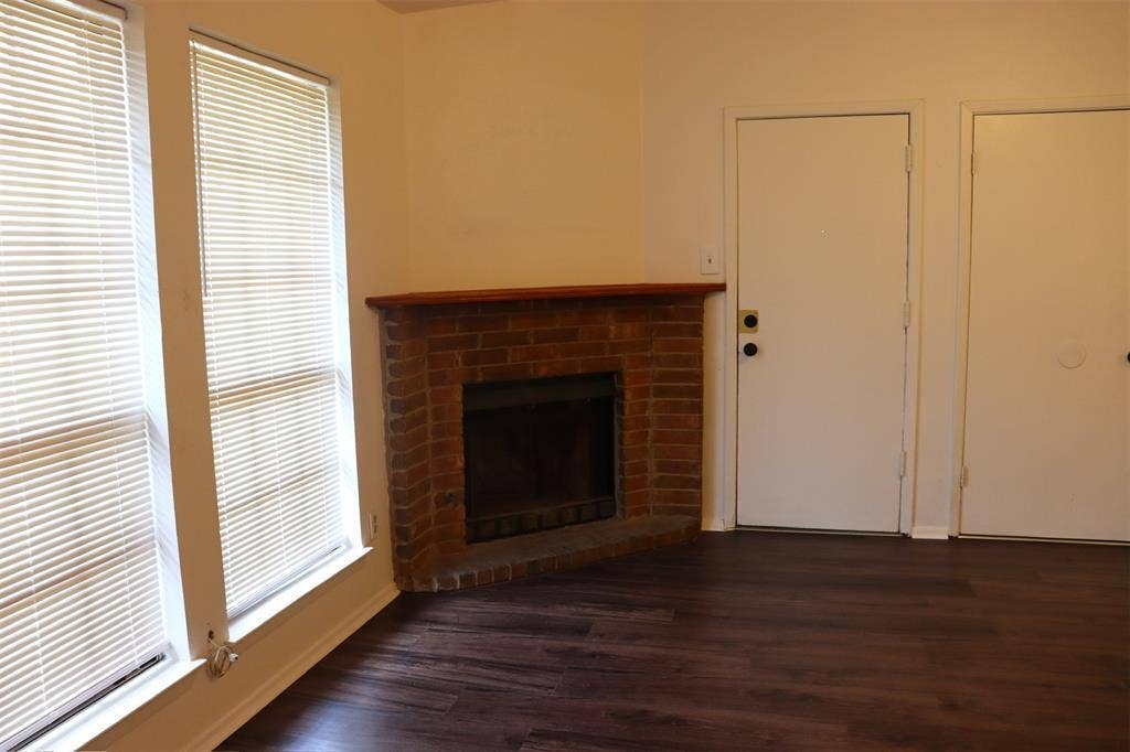 10020 Redondo Drive, Dallas, TX 75218 Living area featuring a corner brick fireplace with a wood mantel, dark wood-finish flooring, and two windows with blinds