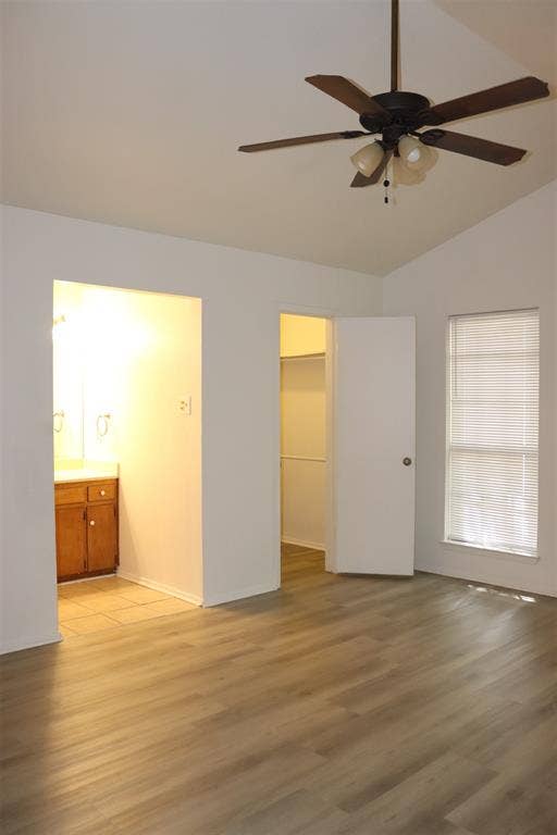 10020 Redondo Drive, Dallas, TX 75218 Spacious room featuring vaulted ceilings, wood-finish flooring, a ceiling fan with light kit, a window with blinds, and an entryway to a bathroom with a wood vanity