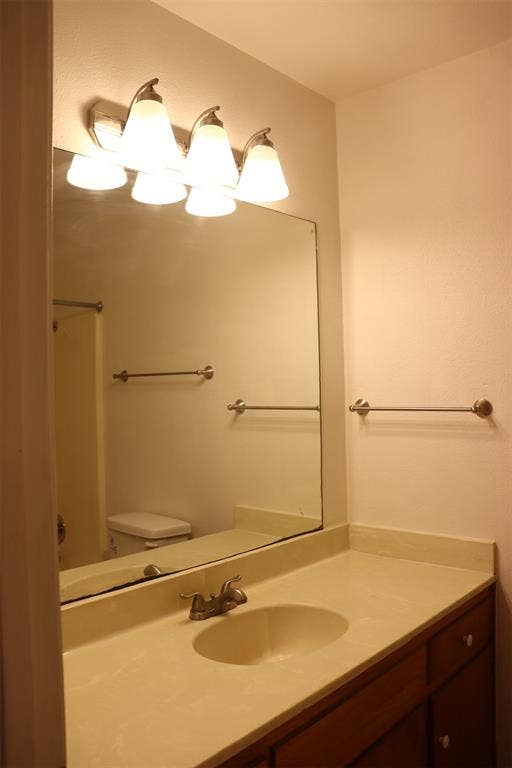 10020 Redondo Drive, Dallas, TX 75218 Bathroom vanity featuring a light-colored countertop, integrated sink, and wood-finish cabinetry