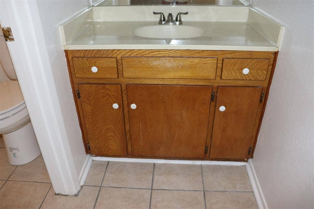 10020 Redondo Drive, Dallas, TX 75218 Bathroom vanity featuring a wood-finish cabinet with white knobs, a light-toned countertop, and an integrated sink with a chrome faucet
