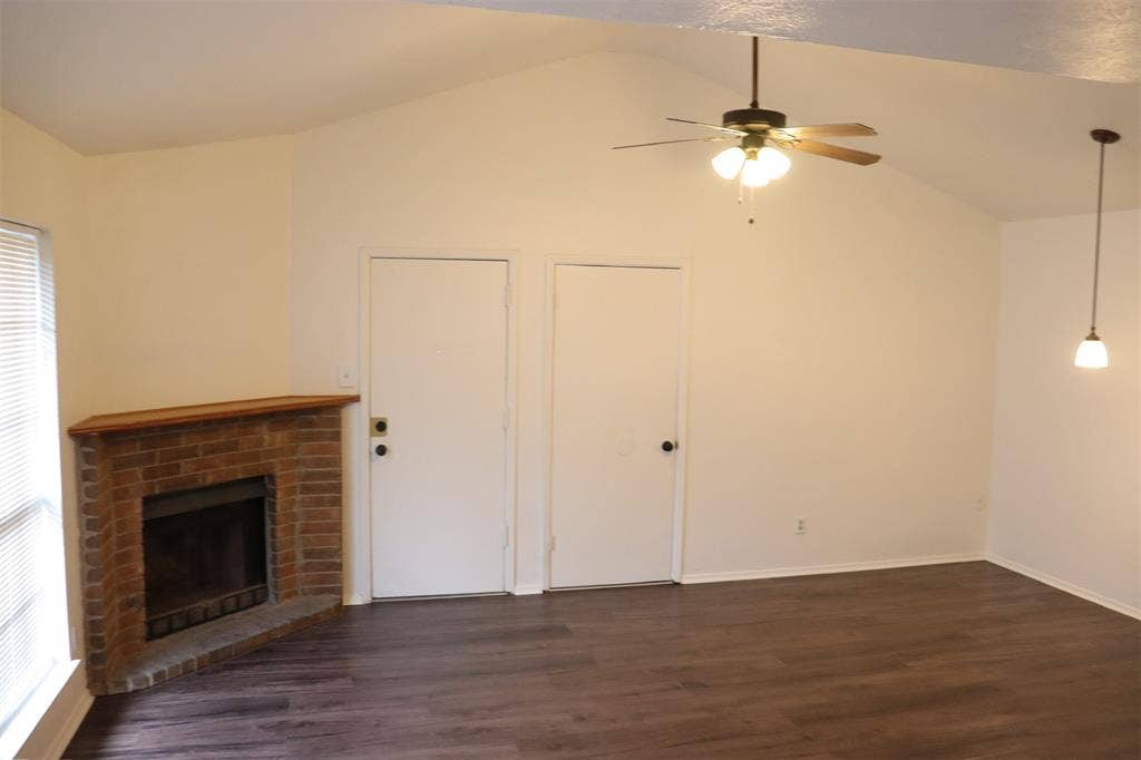 10020 Redondo Drive, Dallas, TX 75218 Living area featuring a brick fireplace with a wood mantel, wood-finish flooring, and a vaulted ceiling