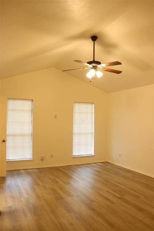 10020 Redondo Drive, Dallas, TX 75218 Spacious room featuring vaulted ceilings, wood-finish flooring, two large windows with blinds, and a ceiling fan with integrated lighting