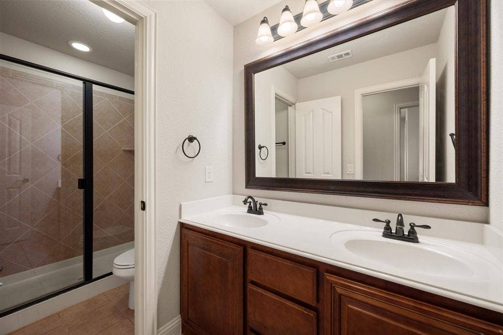 Bathroom featuring a dual-sink vanity with white countertops, dark wood cabinetry, and a framed mirror
