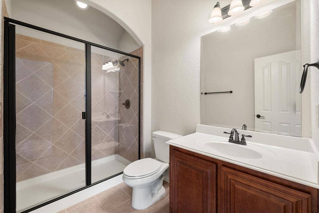 Full bathroom featuring a shower with dark bronze framed glass enclosure, diagonal tile surround, built-in shelving, and dark bronze fixtures