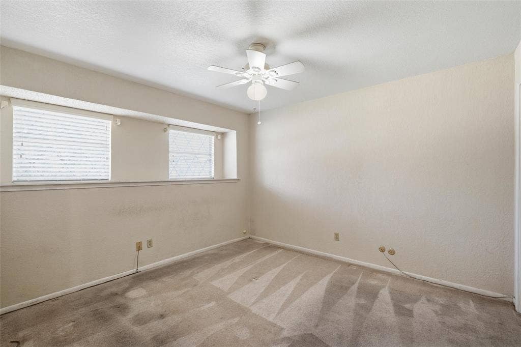 Carpeted room with a ceiling fan, two upper windows with blinds, and neutral-toned walls