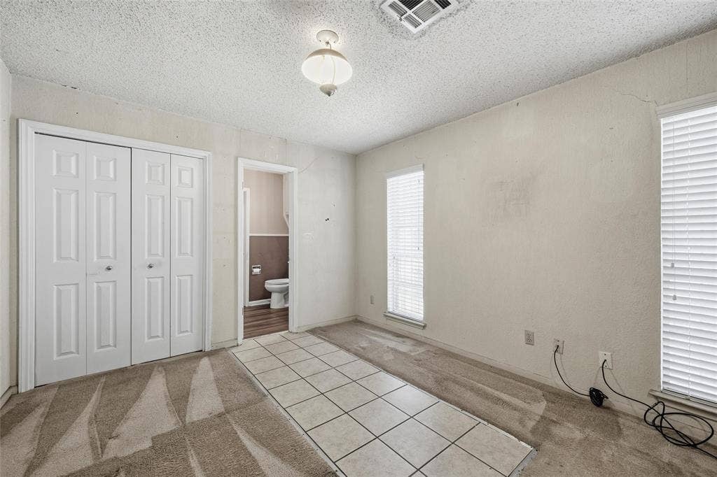 Carpeted room with a central tiled pathway, featuring bi-fold closet doors and multiple windows with horizontal blinds