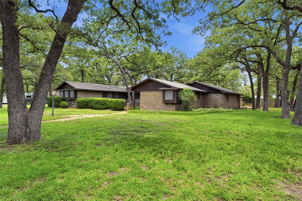 Expansive green lawn surrounds a brick and wood-sided residence