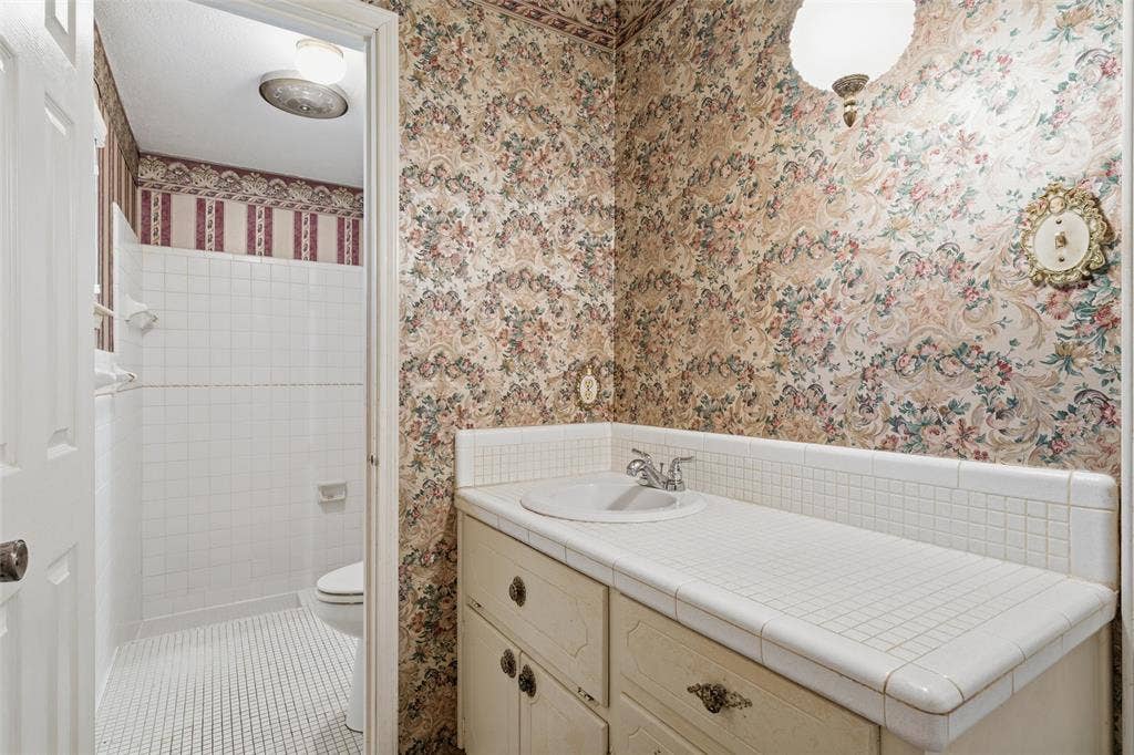 Bathroom featuring a vanity with an integrated sink, tile countertop, and floral wallpaper