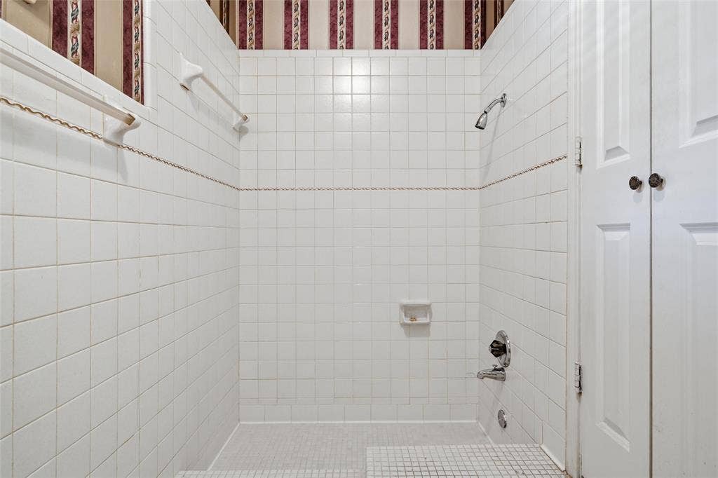 Tiled shower enclosure featuring white square tile walls, a mosaic tile floor, and a shower head with a separate tub spout