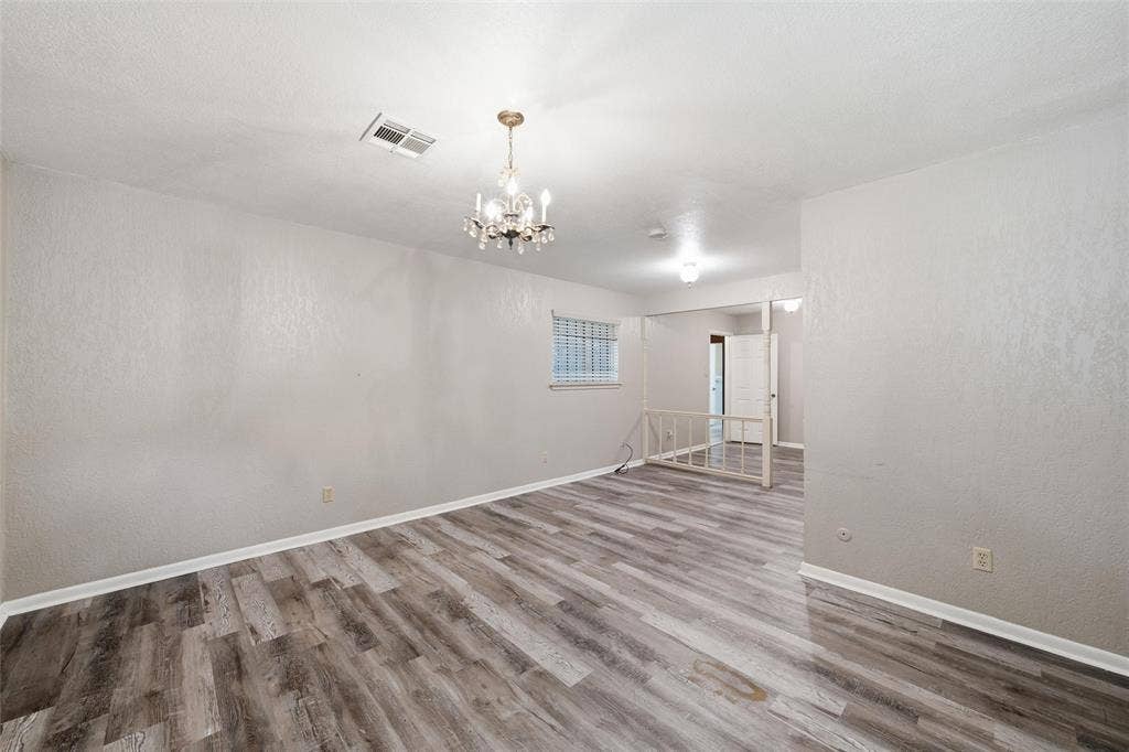 Spacious interior room featuring wood-finish flooring, a decorative chandelier, and white wall finishes