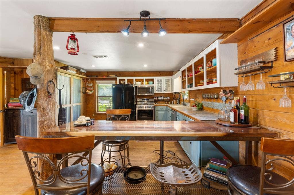 13494 County Road 2919, Eustace, TX 75124 Kitchen featuring wood-paneled walls, a natural wood beam, track lighting, light blue lower cabinetry, white open upper shelving, and a dark wood-finish countertop