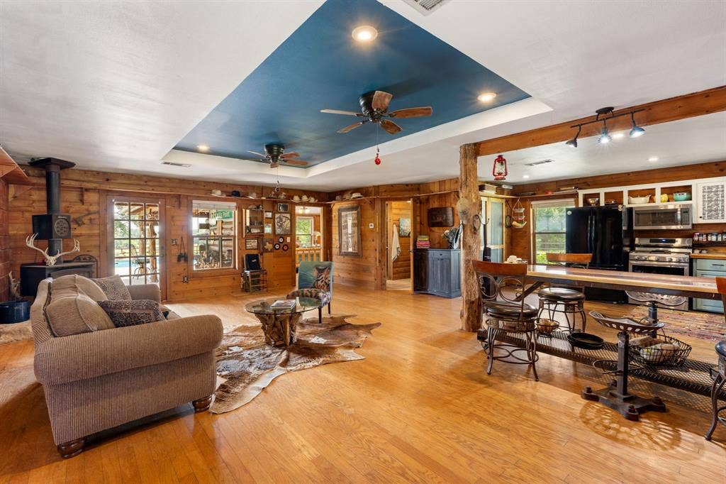 13494 County Road 2919, Eustace, TX 75124 Open-concept living space featuring wood-finish flooring, wood plank walls, and a blue tray ceiling with recessed lighting