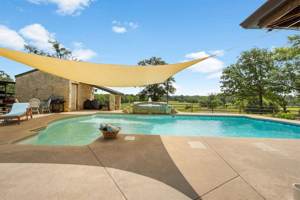 13494 County Road 2919, Eustace, TX 75124 In-ground swimming pool with a concrete deck, an integrated water feature, and a stone-clad pool house