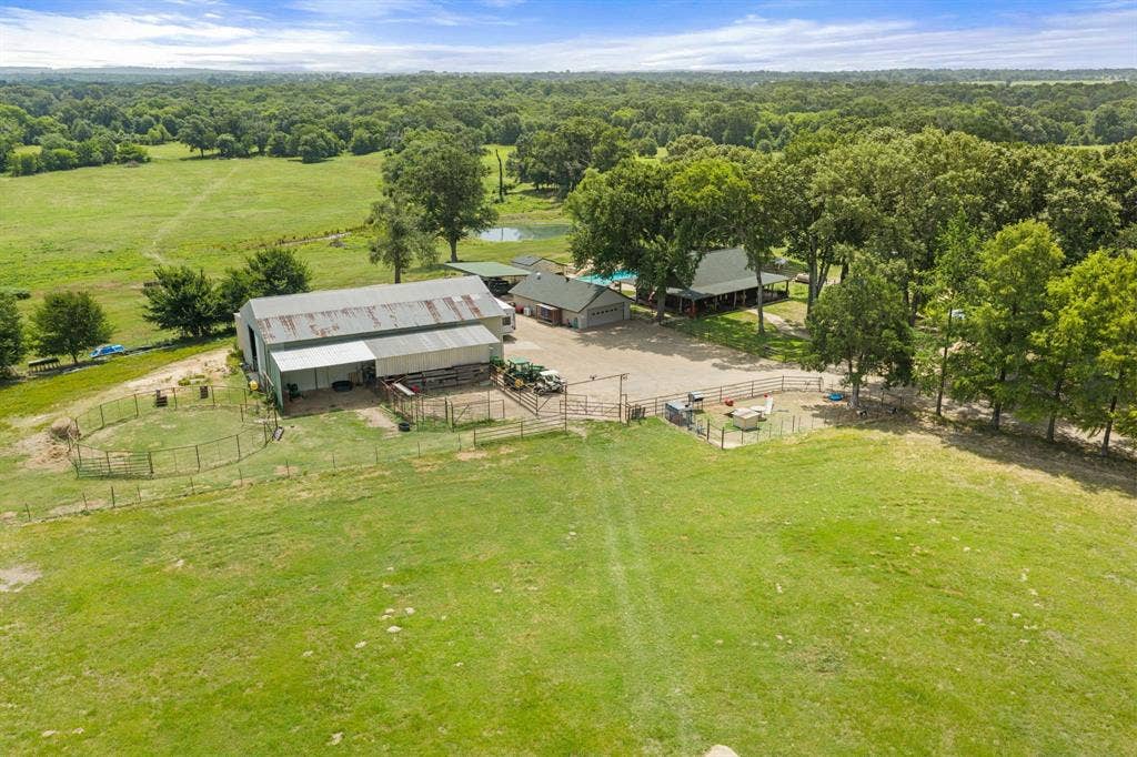 13494 County Road 2919, Eustace, TX 75124 Expansive property featuring a large barn with an attached lean-to, multiple fenced enclosures, a separate building with a green roof, and a visible pond surrounded by mature trees