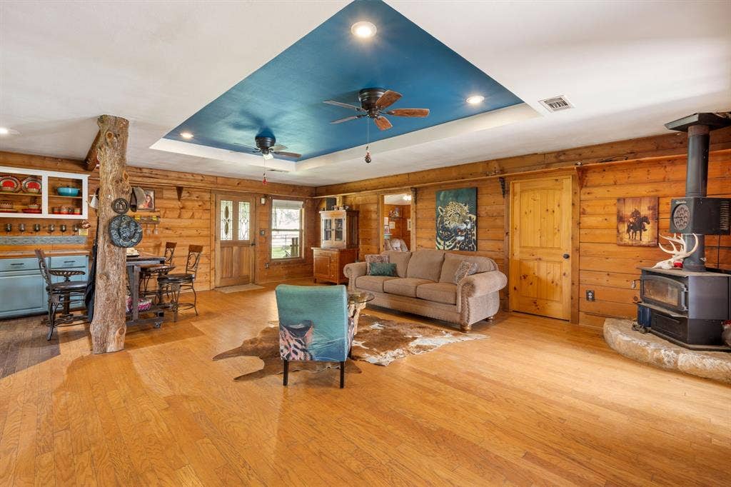 13494 County Road 2919, Eustace, TX 75124 Spacious living area featuring wood-finish flooring, wood-paneled walls, and a recessed ceiling with a blue accent panel