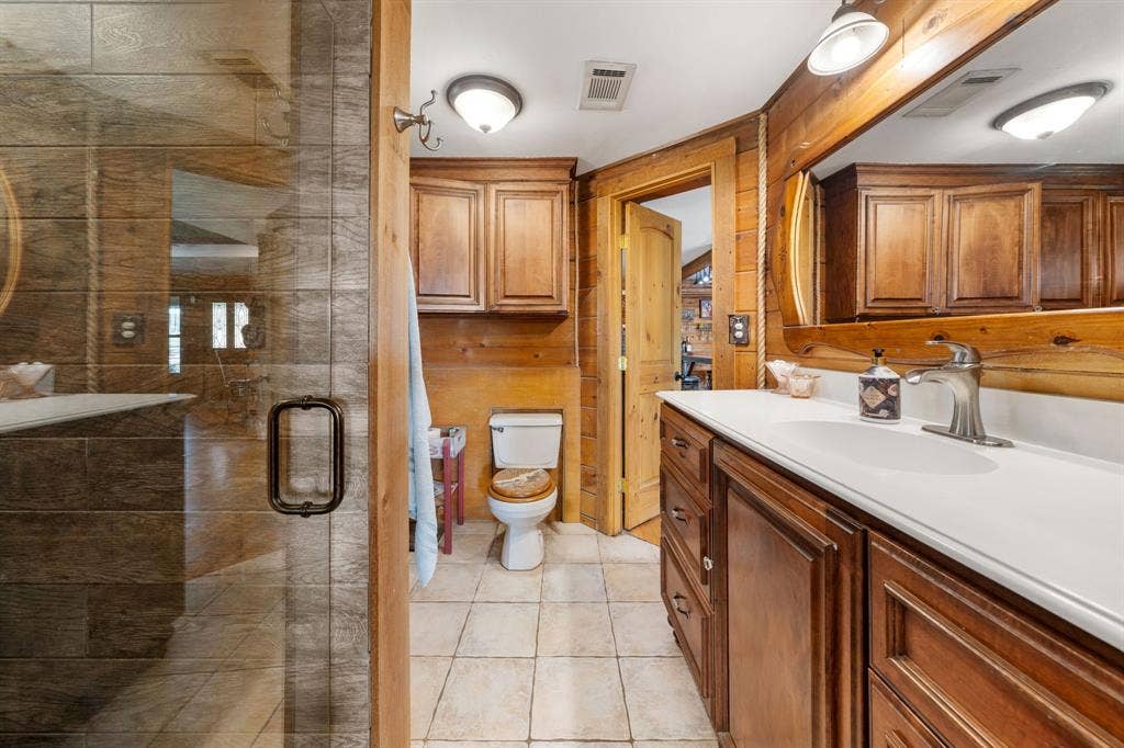 13494 County Road 2919, Eustace, TX 75124 Bathroom featuring a clear glass shower enclosure, wood-paneled walls, a single vanity with a white countertop and dark wood cabinetry, and tiled flooring
