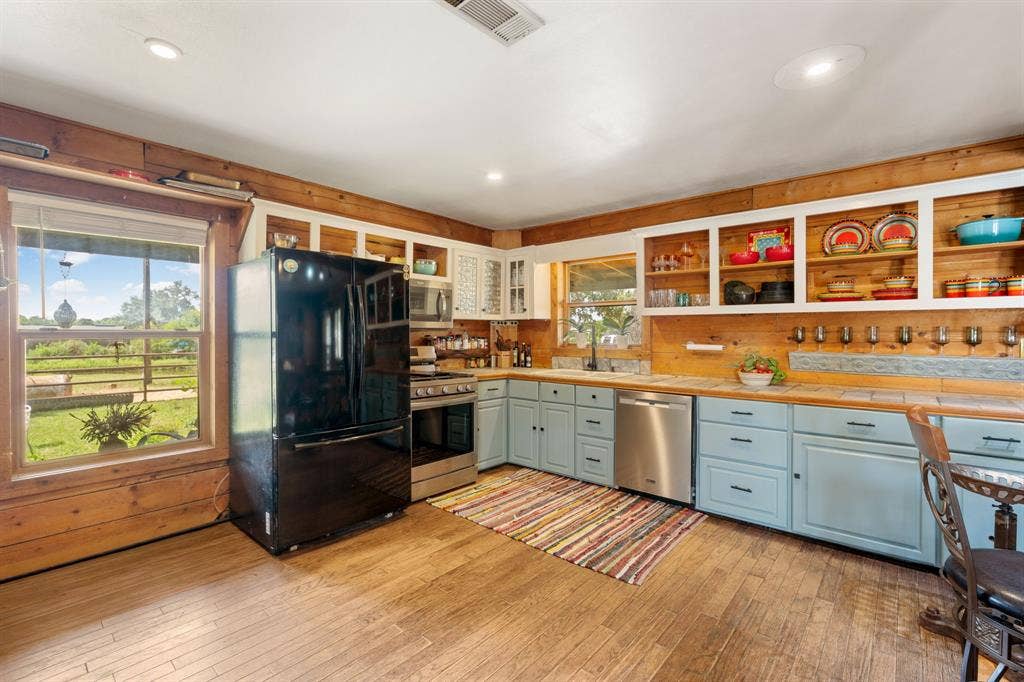 13494 County Road 2919, Eustace, TX 75124 Kitchen featuring wood-finish flooring, wood plank walls, light blue lower cabinetry, stainless steel appliances, and open shelving