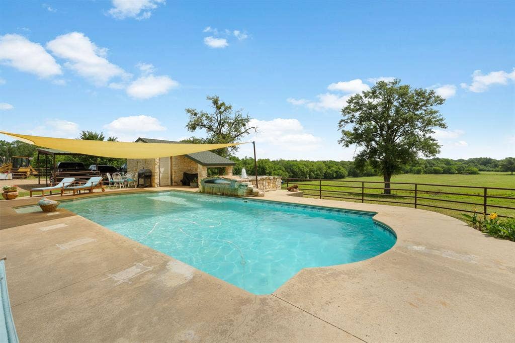13494 County Road 2919, Eustace, TX 75124 Outdoor pool with expansive concrete decking, stone-clad outdoor kitchen structure, and a secondary spa feature