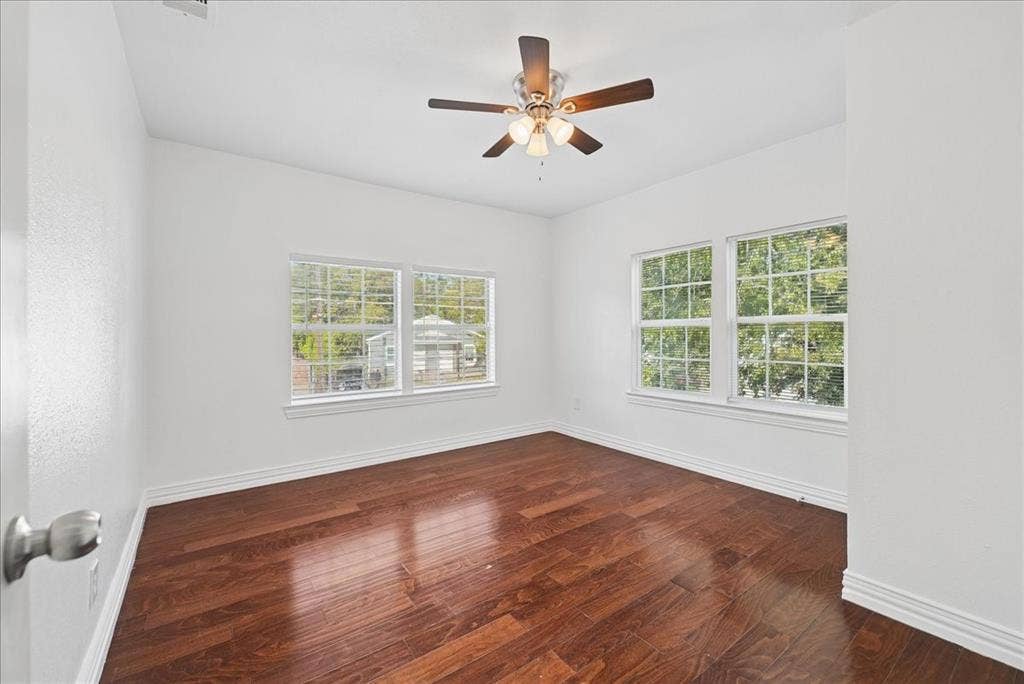 Hardwood-style flooring, white trim, multiple windows, and a ceiling fan